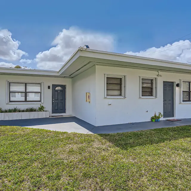 Exterior view of a white residential building with a landscaped lawn and two front doors.