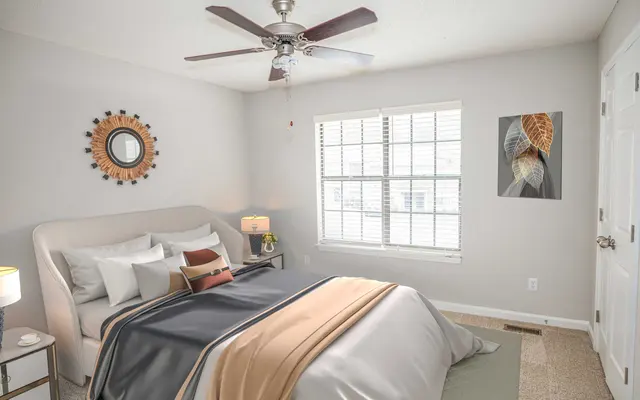 Summit at 501 Modern bedroom with a large bed, decorative mirror, window with blinds, and wall art. Soft color palette enhances tranquility.