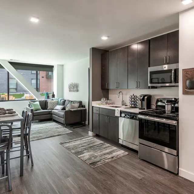 Syracuse, NY Pet-Friendly Student Apartments - 505 on Walnut - Kitchen with Upgraded Wood-Style Flooring, Stainless-Steel Appliances, Dark Wooden Cabinets, and Granite-Style Countertops, and View of Dining and Living Areas.

