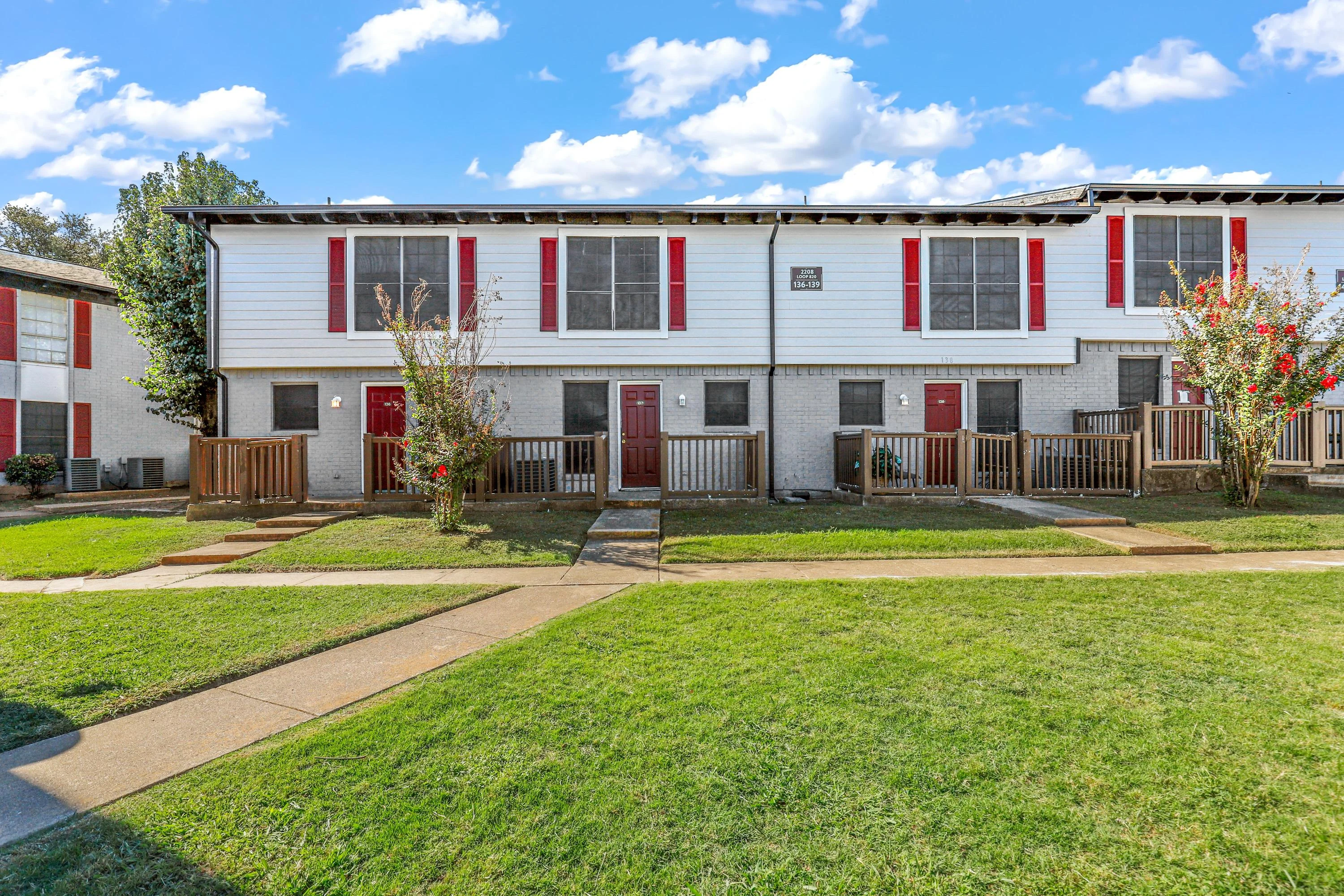Exterior view of a two-story residential building with multiple units, featuring green grass and a pathway.