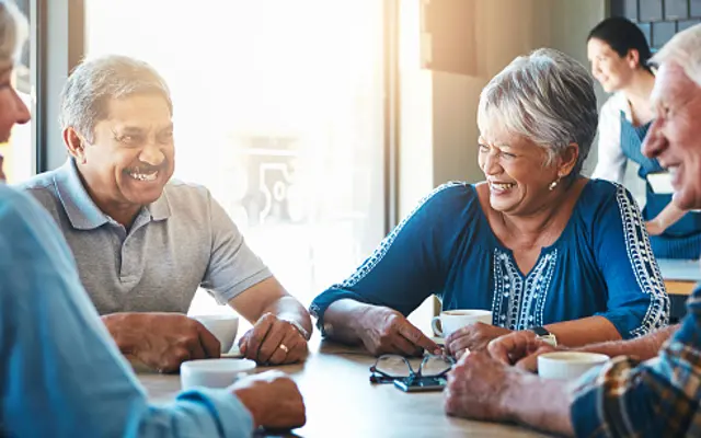 Friends Gathering for Coffee A group of four older adults sitting around a table in a bright café, laughing and enjoying each other's company over cups of coffee.