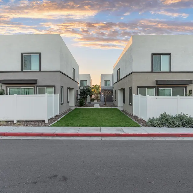 Modern Houses on a Sunset Evening A symmetrical view of two modern houses with light-colored exteriors, separated by a green lawn and a pathway, under a colorful sunset sky.
