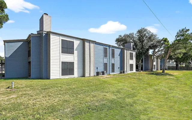 Exterior view of an apartment complex with a green lawn and trees.