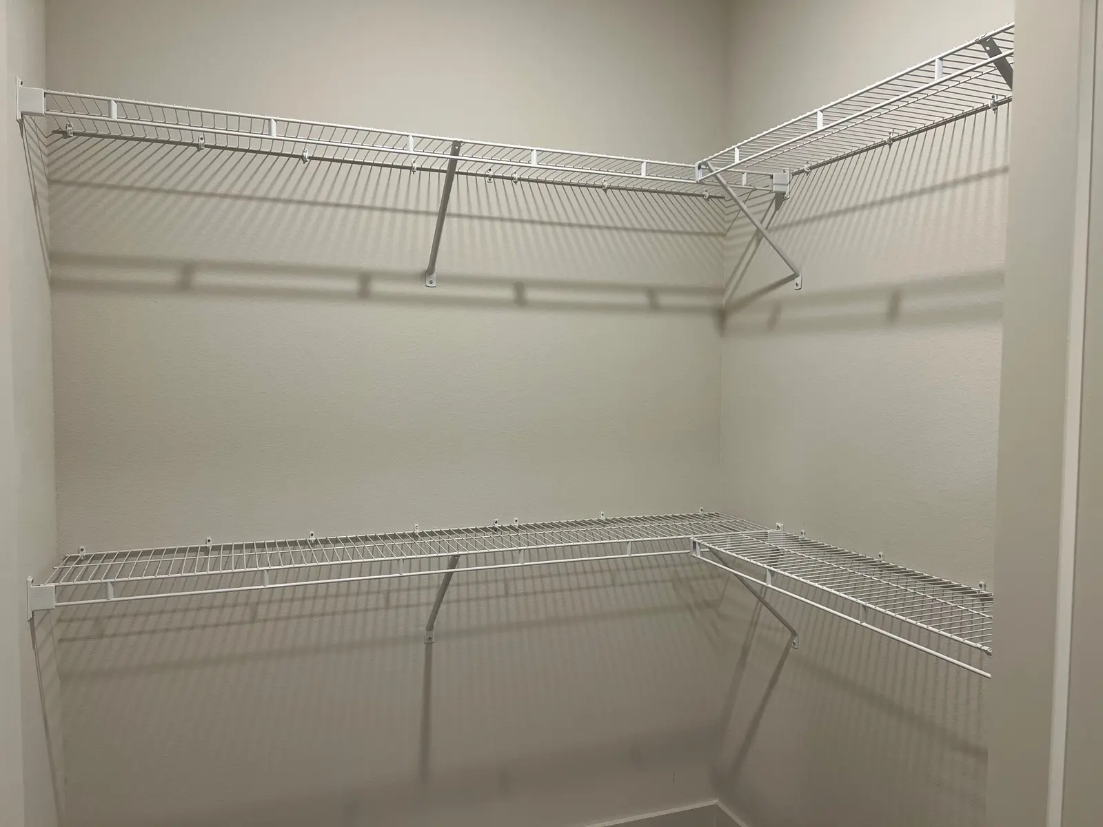 Empty Closet with Wire Shelving An empty closet with white wire shelving installed on two walls, showcasing a spacious and organized layout.