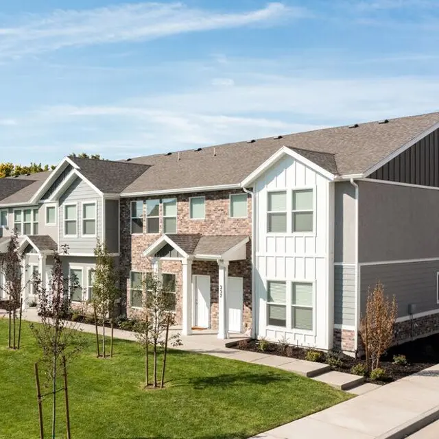 A modern residential building complex with multiple units, featuring a mix of brick and siding exteriors, well-maintained lawns, and newly planted trees.