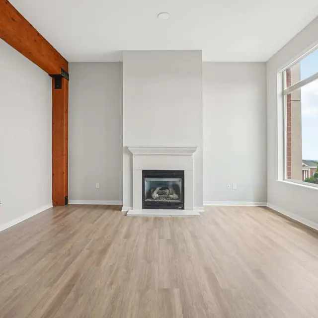 Contemporary Living Room Design A bright and airy living room featuring a modern fireplace, large windows with city views, and a light wooden floor. The walls are painted in a soft gray color, and there is a wooden beam accent on the ceiling.