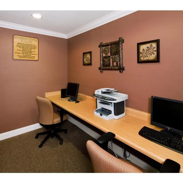 Cozy Office Space A small office area with two computer workstations, a printer, and decorative wall art. The walls are painted in a warm brown color, and there is a plant in the corner.