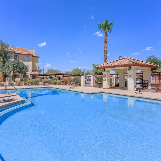 Resort Pool Area A clear blue swimming pool surrounded by palm trees and lounge chairs, with a shaded area featuring tables and chairs.