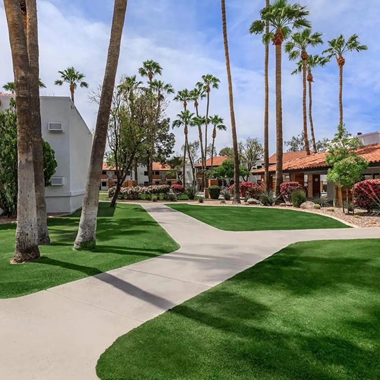 A green landscaped area with palm trees and a concrete pathway in an apartment complex.
