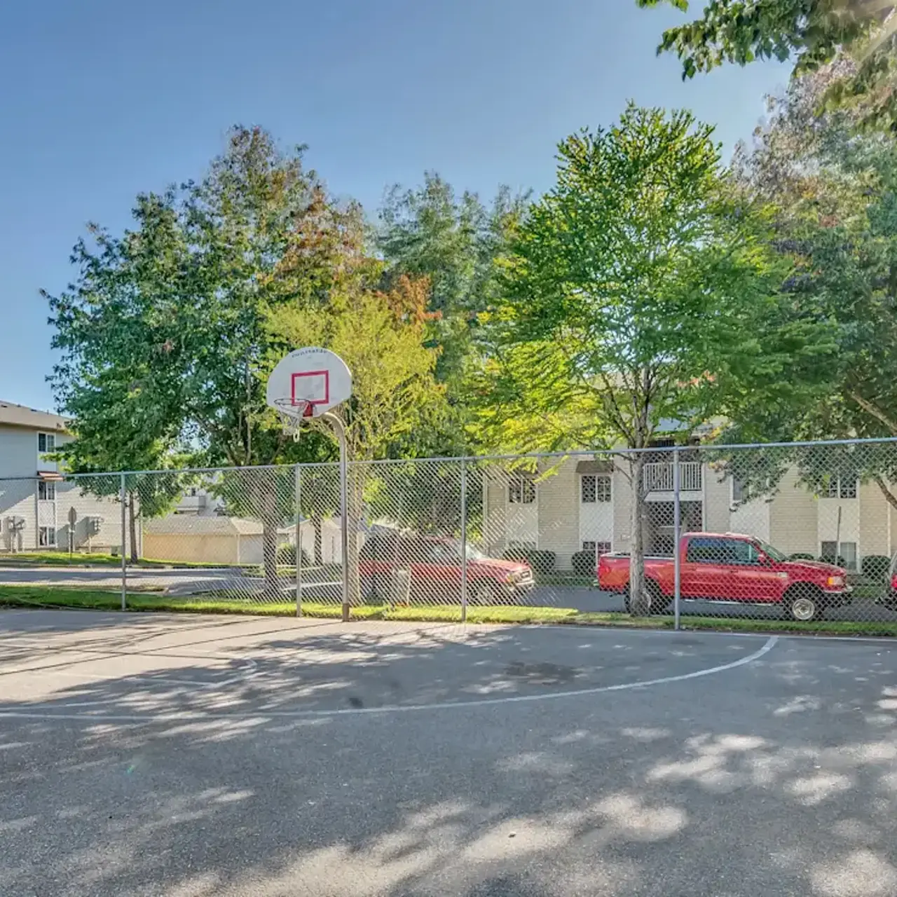 A fenced basketball court surrounded by trees and residential buildings.