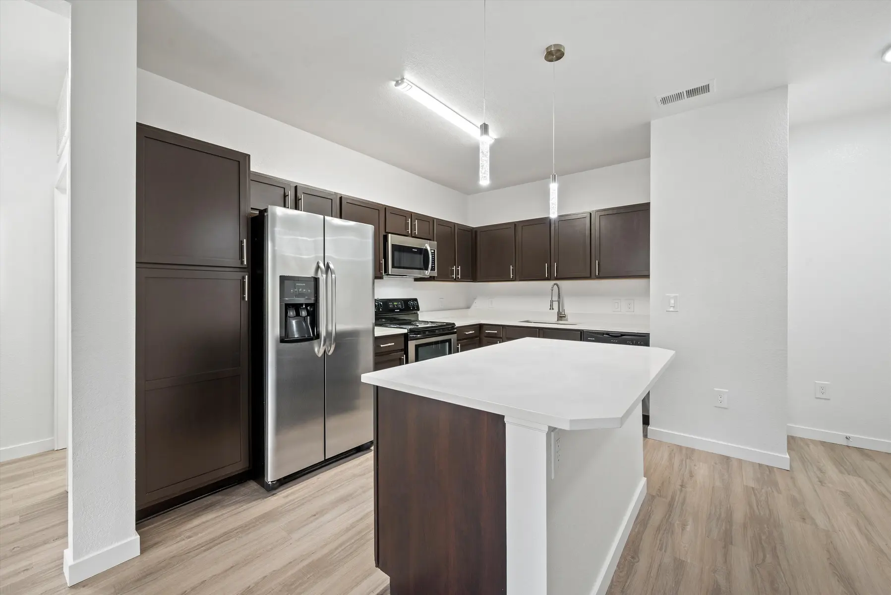 A modern kitchen featuring dark wood cabinets, stainless steel appliances, and a center island with a white countertop.