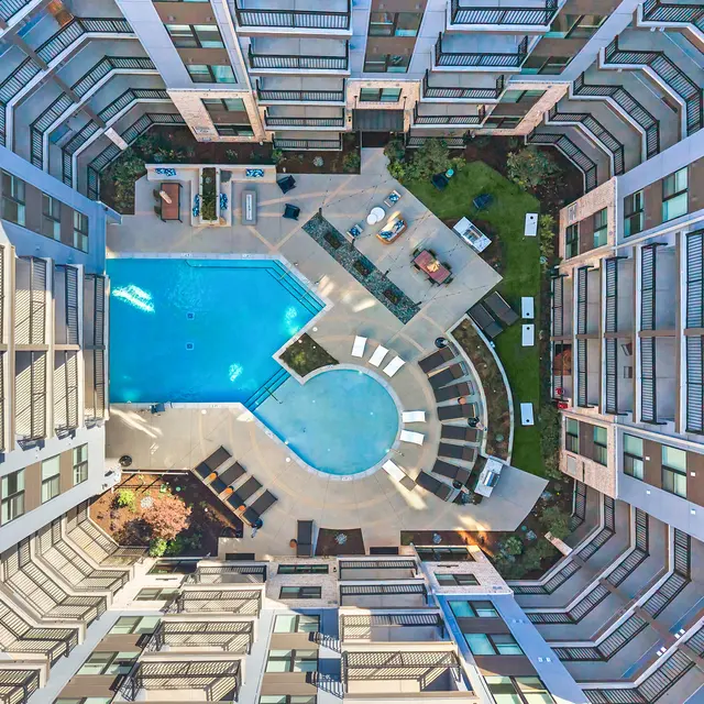 Aerial view of a modern apartment complex featuring a swimming pool in the center, surrounded by buildings and landscaped areas.