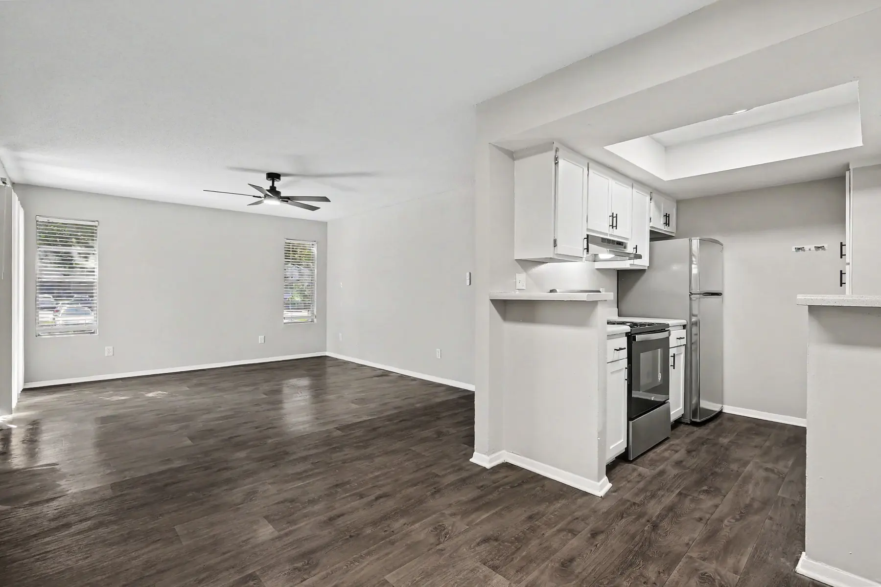 Open concept living area with kitchen and living room in a modern apartment, featuring wood-style flooring and neutral paint colors.