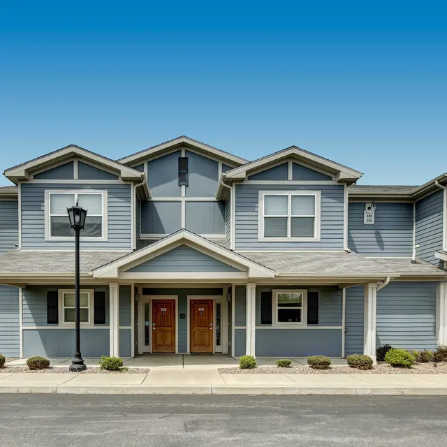 Front view of a two-story residential building with a gray exterior and a landscaped walkway.