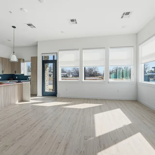 Bright, modern kitchen and living area with large windows, light wood floors, and a minimalist design. Sunlight streaming in.
