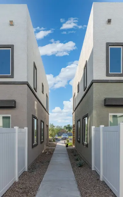 Pathway Between Modern Homes A pathway between two modern homes with a white picket fence, under a clear blue sky adorned with scattered clouds.
