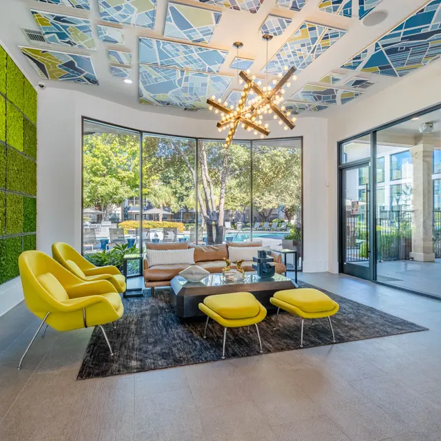 A modern lobby featuring a green wall, bright yellow chairs, and large windows looking out to a pool area.