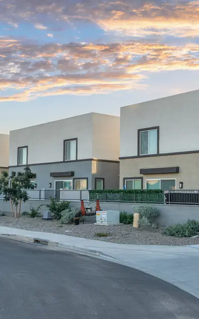 Contemporary Houses at Sunset A row of modern, minimalist houses with flat roofs, set against a colorful sky at sunset. The scene includes greenery and a well-paved road.