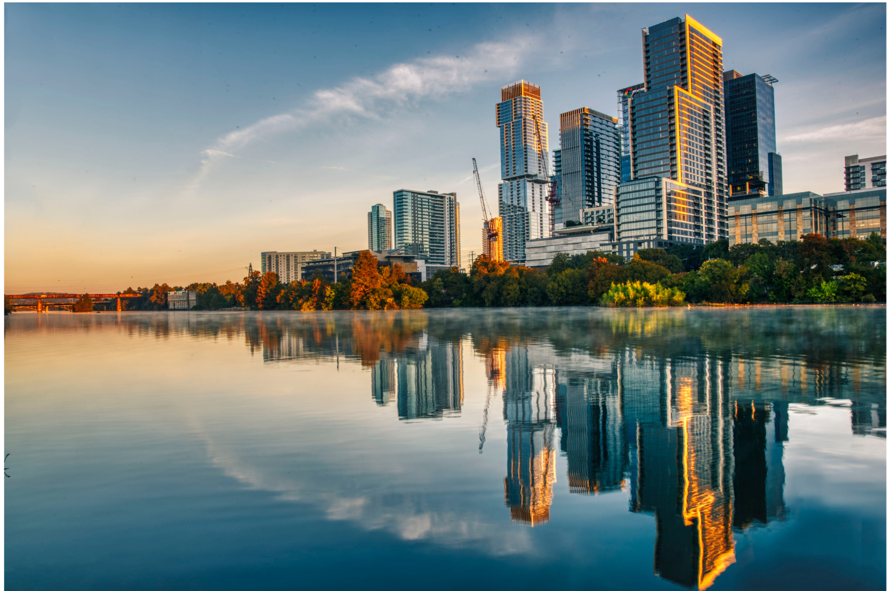 City Skyline at Dawn A skyline of tall buildings reflecting on a calm body of water during sunrise.