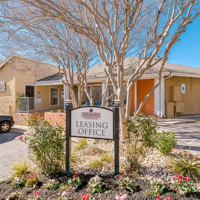 Leasing Office Exterior Exterior view of a leasing office with a sign in front, surrounded by landscaping and paved parking spaces.