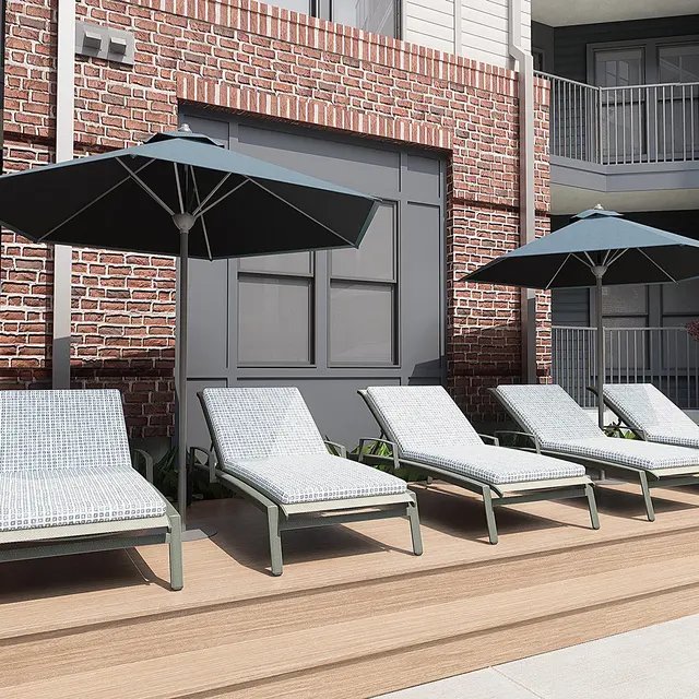 Lounge chairs with umbrellas on a wooden deck next to a brick building.