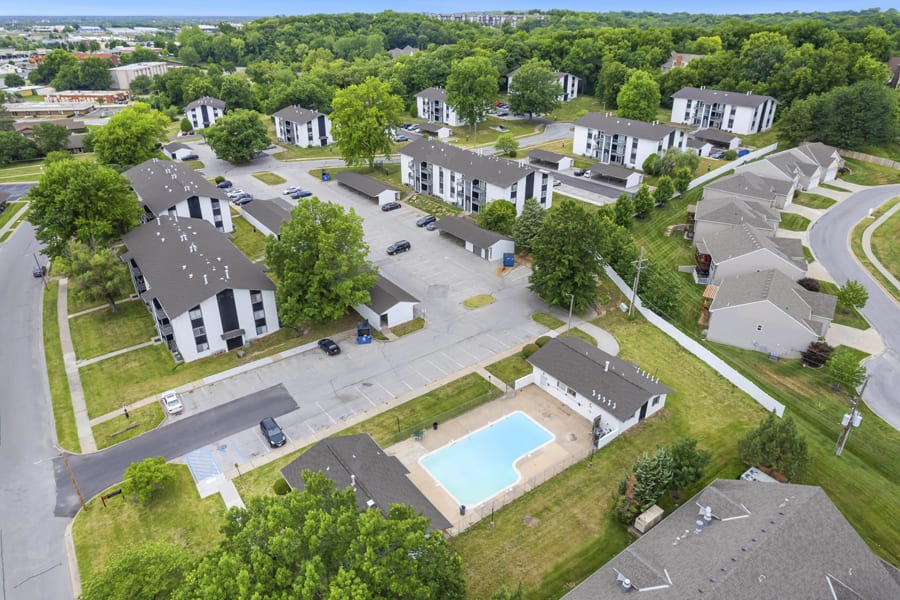 Aerial View of Apartment Complex Aerial view of an apartment complex with multiple buildings and a swimming pool amidst green trees and landscaped areas.