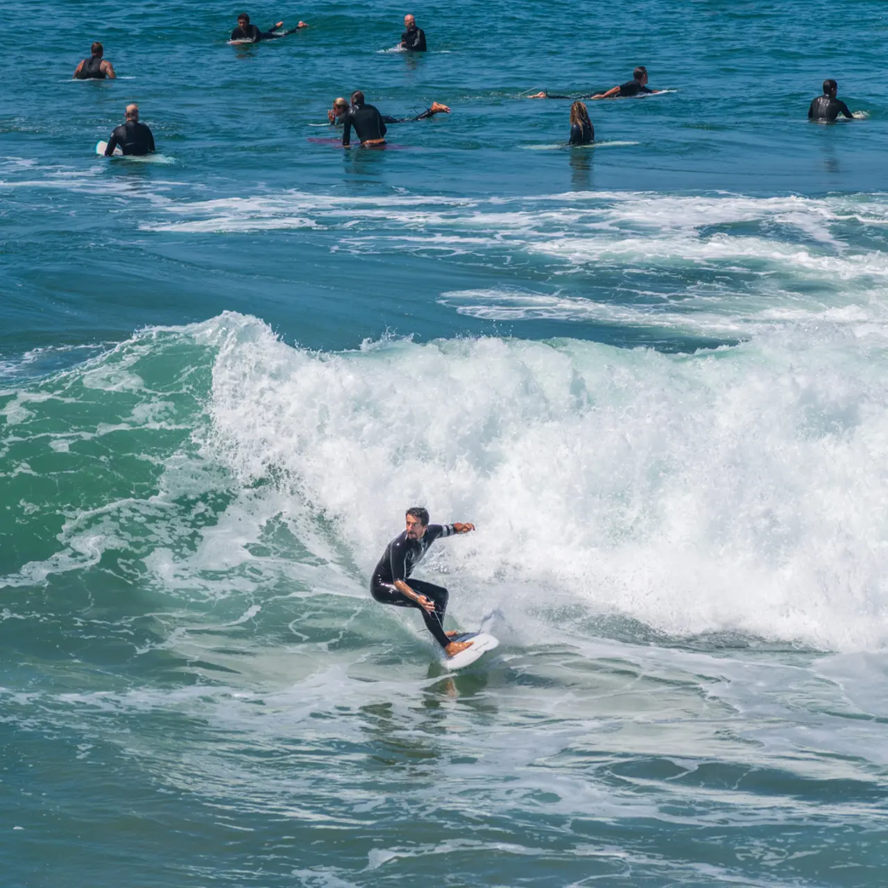 A surfer riding a wave in the ocean with several surfers in the background waiting or paddling on their boards.