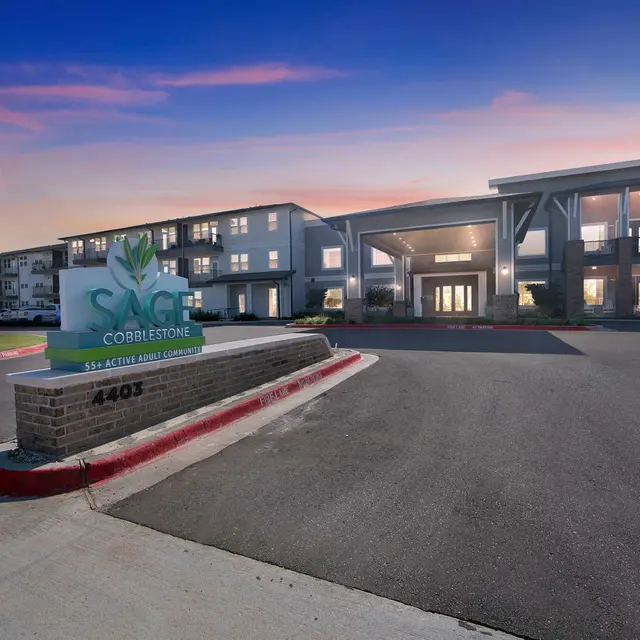 Modern apartment building with a welcoming entrance, landscaped surroundings, and a sign reading "SAGE Cobblestone" at sunset.