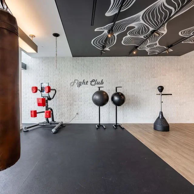 An interior view of a modern fight club gym featuring a punching bag, boxing equipment, and training dummies against stylish decor.