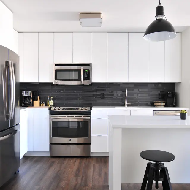 Vernon Court - Kitchen Modern kitchen with sleek white cabinets, stainless steel appliances, and dark accents, featuring a minimalist design and bar stools.