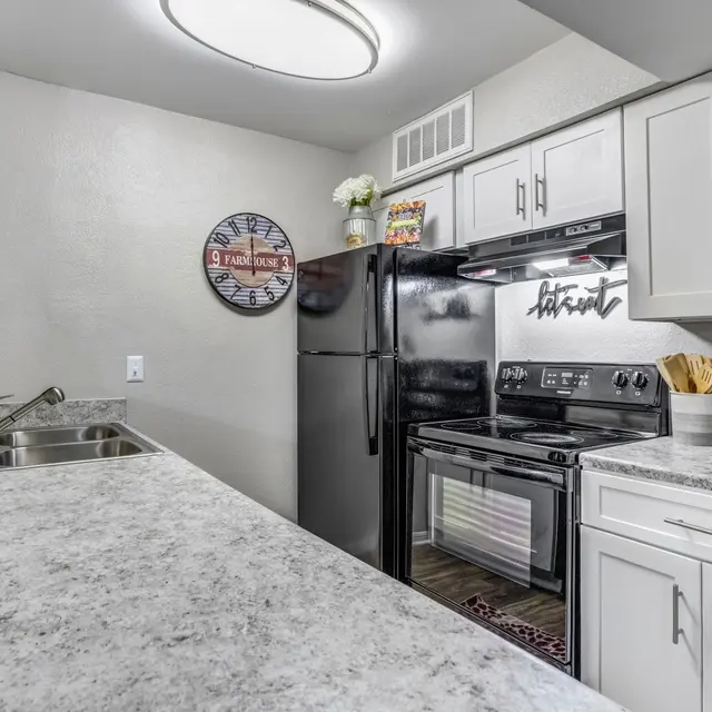 Modern kitchen with dark appliances, grey cabinets, a granite countertop, and a wall clock. Decor items add a cozy touch.
