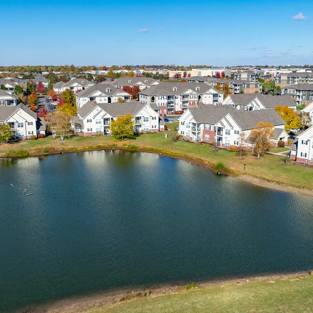 Aerial view of a residential community surrounding a calm lake, with autumn foliage and blue skies.