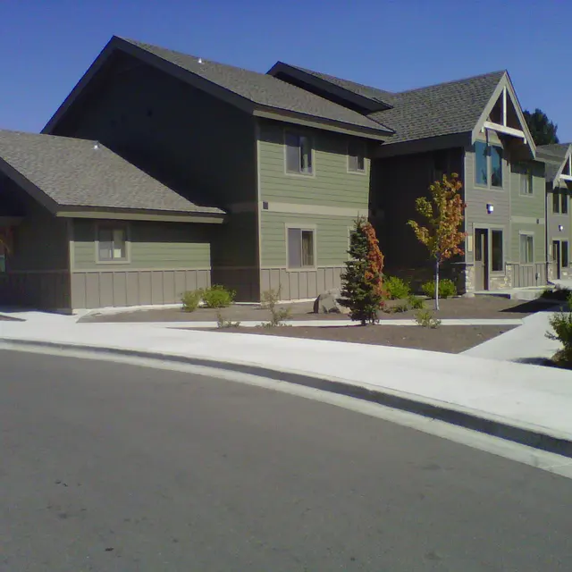 Modern Apartment Building A modern apartment building with a green exterior and sloped roofs, surrounded by landscaping and pavement.