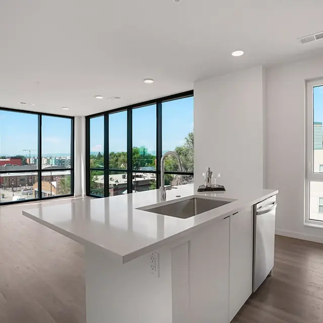 A spacious modern apartment interior featuring a kitchen island, large windows, and wooden flooring, with city views visible through the glass.