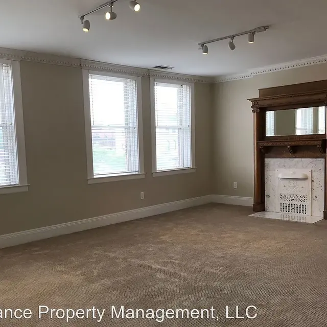 An empty living room featuring a decorative fireplace and large windows allowing natural light.