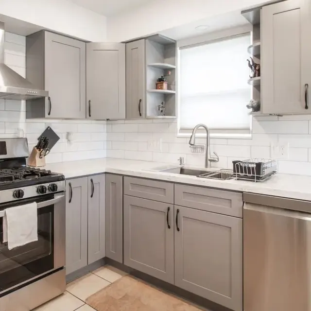 A modern kitchen featuring grey cabinetry, stainless steel appliances, and a clean white tile backsplash.
