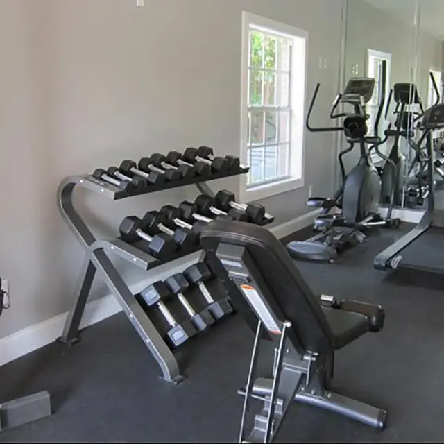 Fitness center with cardio equipment and dumbbell weights racked against the wall next to a window. 