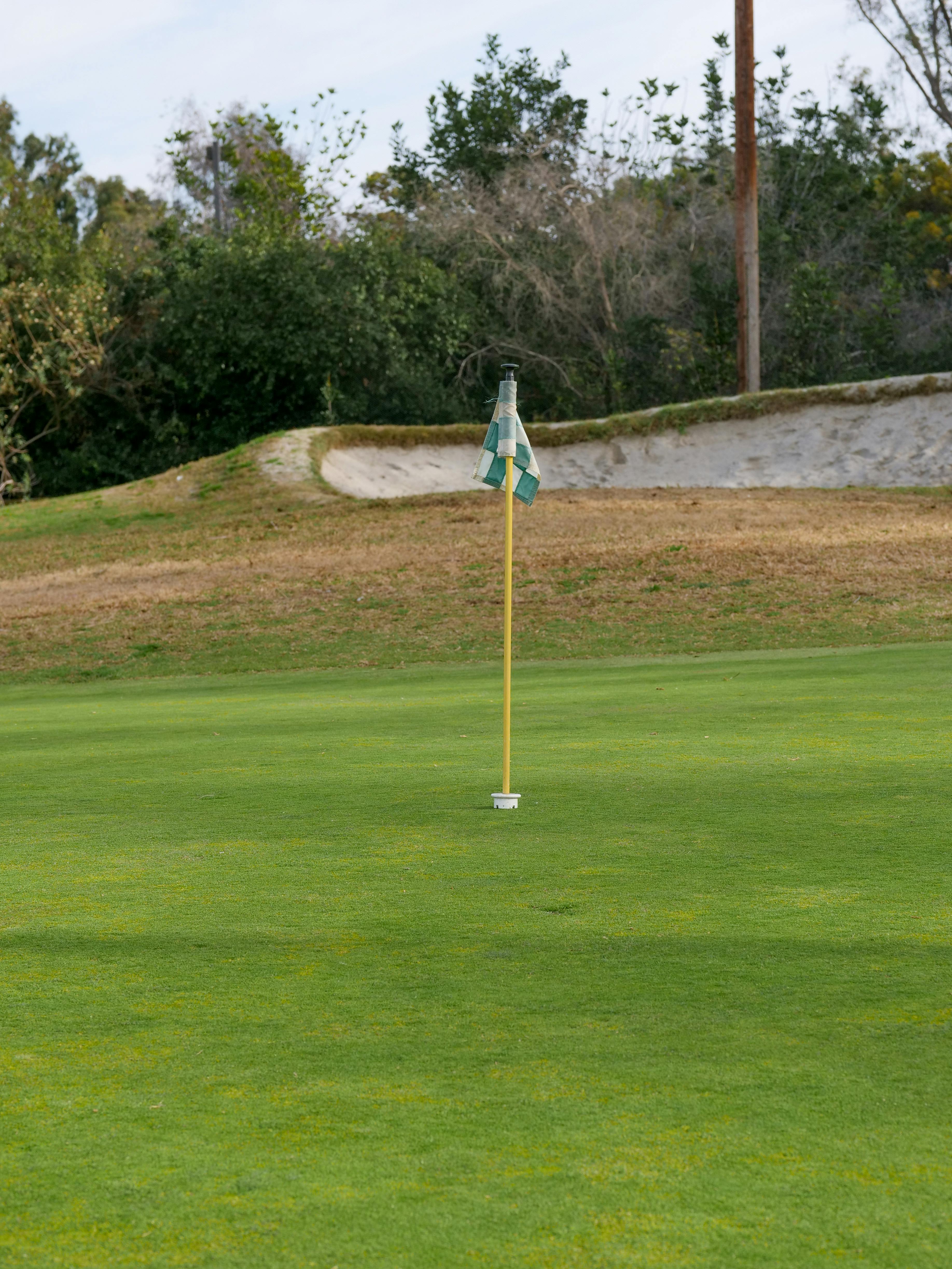 Golf Course Green with Flag A golf course with a visible flag on the green and a sand trap in the background.