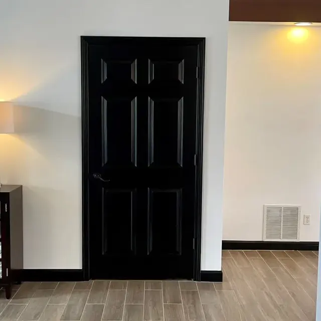 A modern interior entrance area with a black door on the left, a decorative table with a lamp, and a light-colored wall in the background.