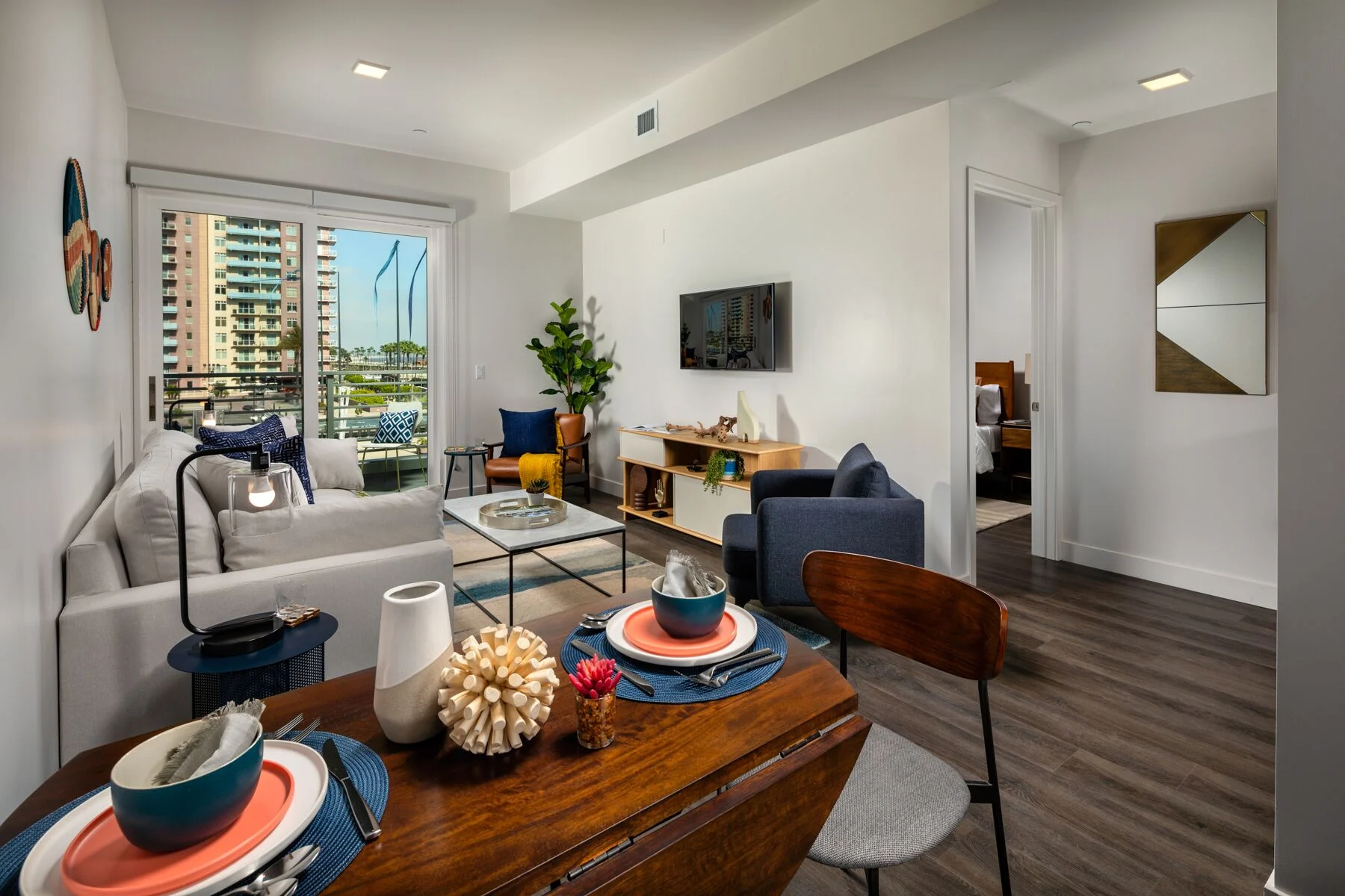 A modern living room with a dining area, featuring a sofa, coffee table, and a view of the city through large windows.