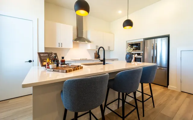 A modern kitchen featuring an island with three bar stools, pendant lighting, and stainless steel appliances.