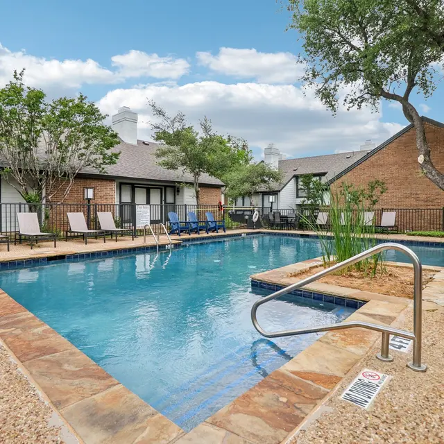 An inviting swimming pool area surrounded by green trees and lounge chairs at an apartment complex.