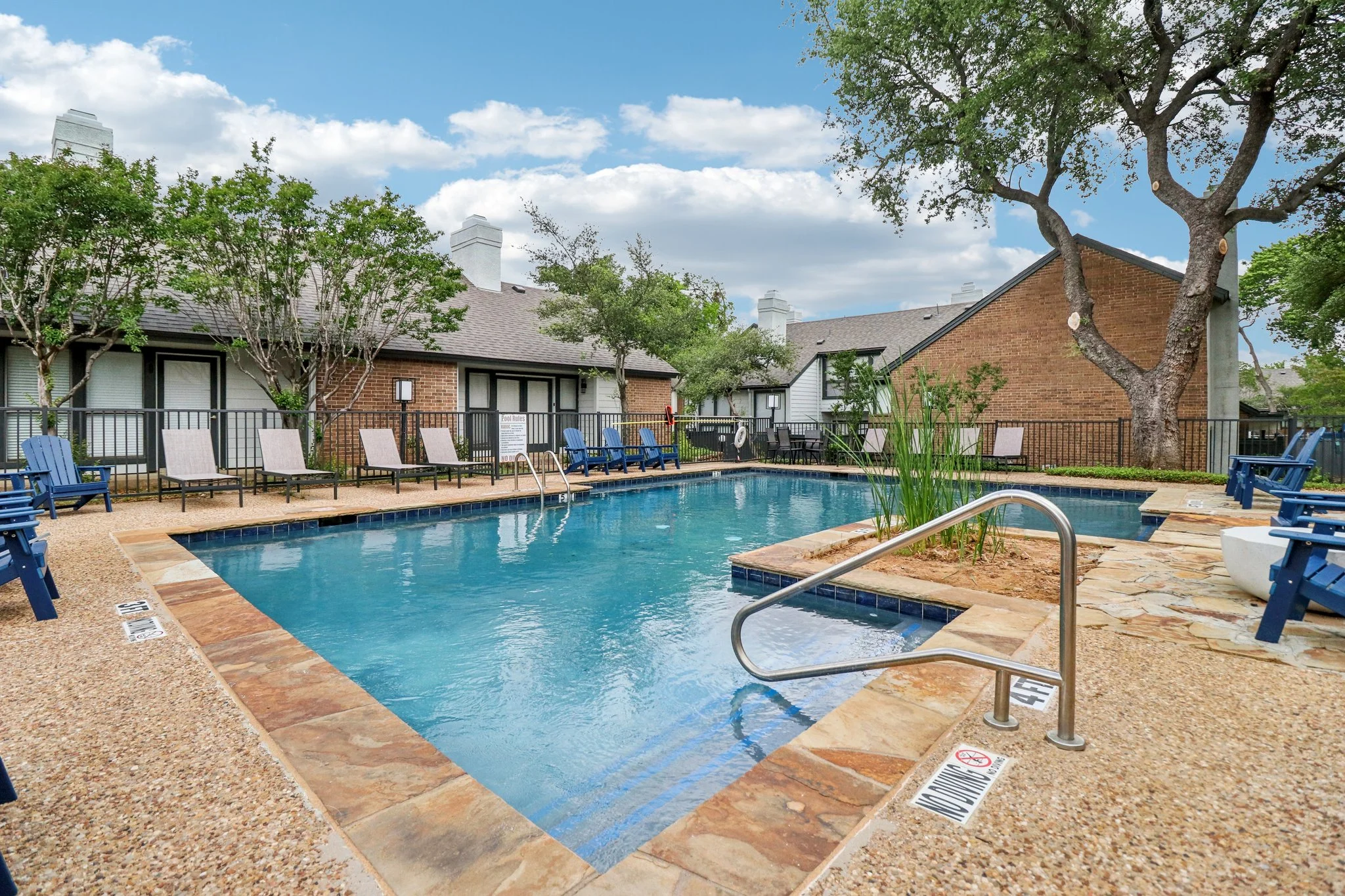 An inviting swimming pool area surrounded by green trees and lounge chairs at an apartment complex.
