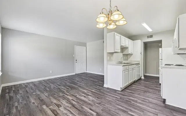 Modern Open Kitchen Space A spacious, modern kitchen with a dining area featuring white cabinetry and hardwood-style flooring. The room has large windows allowing natural light to stream in, and a chandelier hanging from the ceiling.