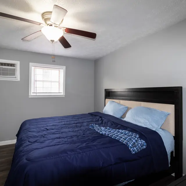 Cozy bedroom featuring a blue bedspread, a ceiling fan, and an air conditioning unit