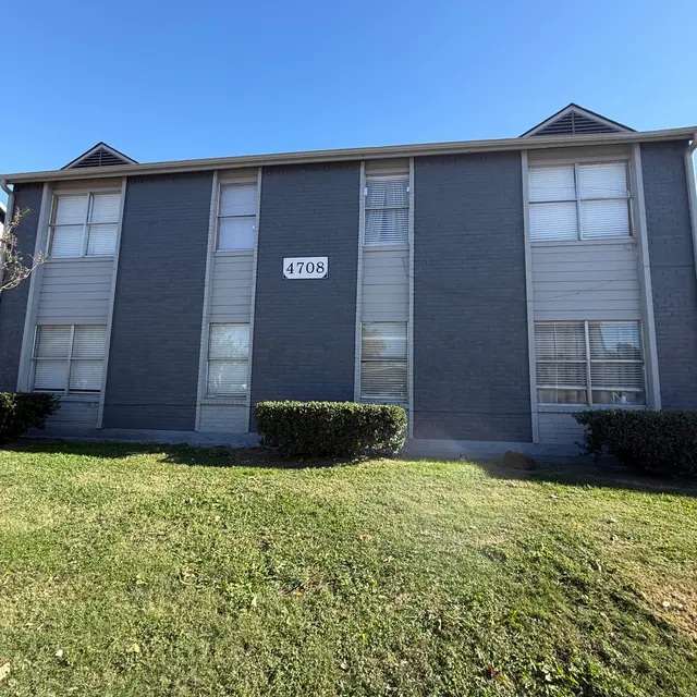 Exterior view of a two-story gray apartment building with large windows and a green lawn in front.