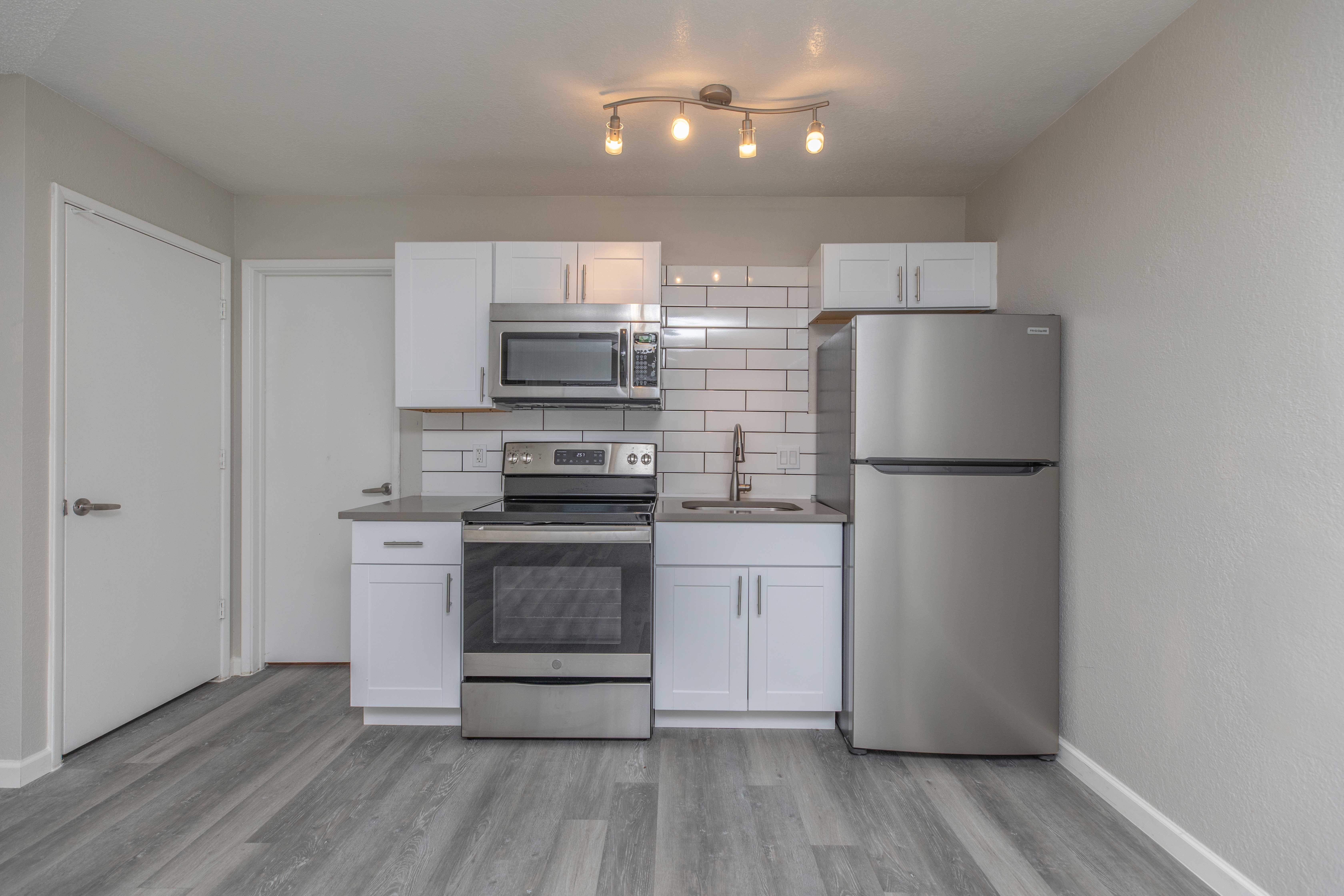 Modern Kitchen Interior A modern kitchen featuring white cabinets, stainless steel appliances including a stove, microwave, and refrigerator, with a backsplash of white tiles. The flooring is a light wood look, and there is overhead lighting.
