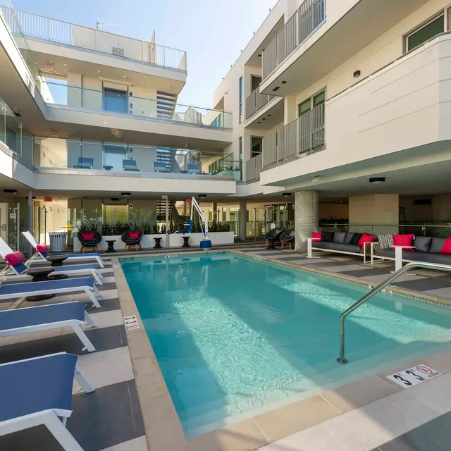 Modern Apartment Pool Area A modern apartment complex featuring a swimming pool surrounded by lounge chairs and colorful cushions, with multiple floors of balconies visible in the background.