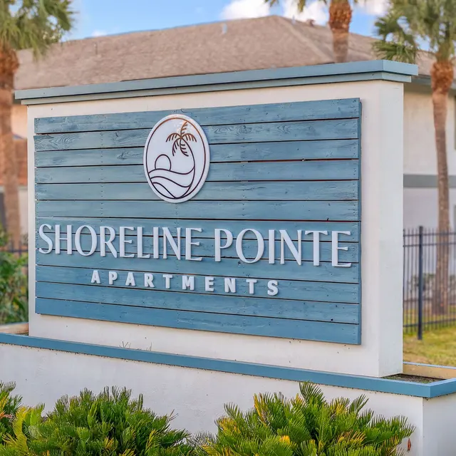 Sign for Shoreline Pointe Apartments with a palm tree logo in a tropical setting.