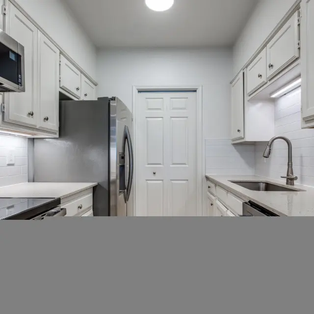 A modern kitchen featuring white cabinetry, stainless steel appliances, and a clean countertop layout. The room has bright lighting and a door leading to another area.